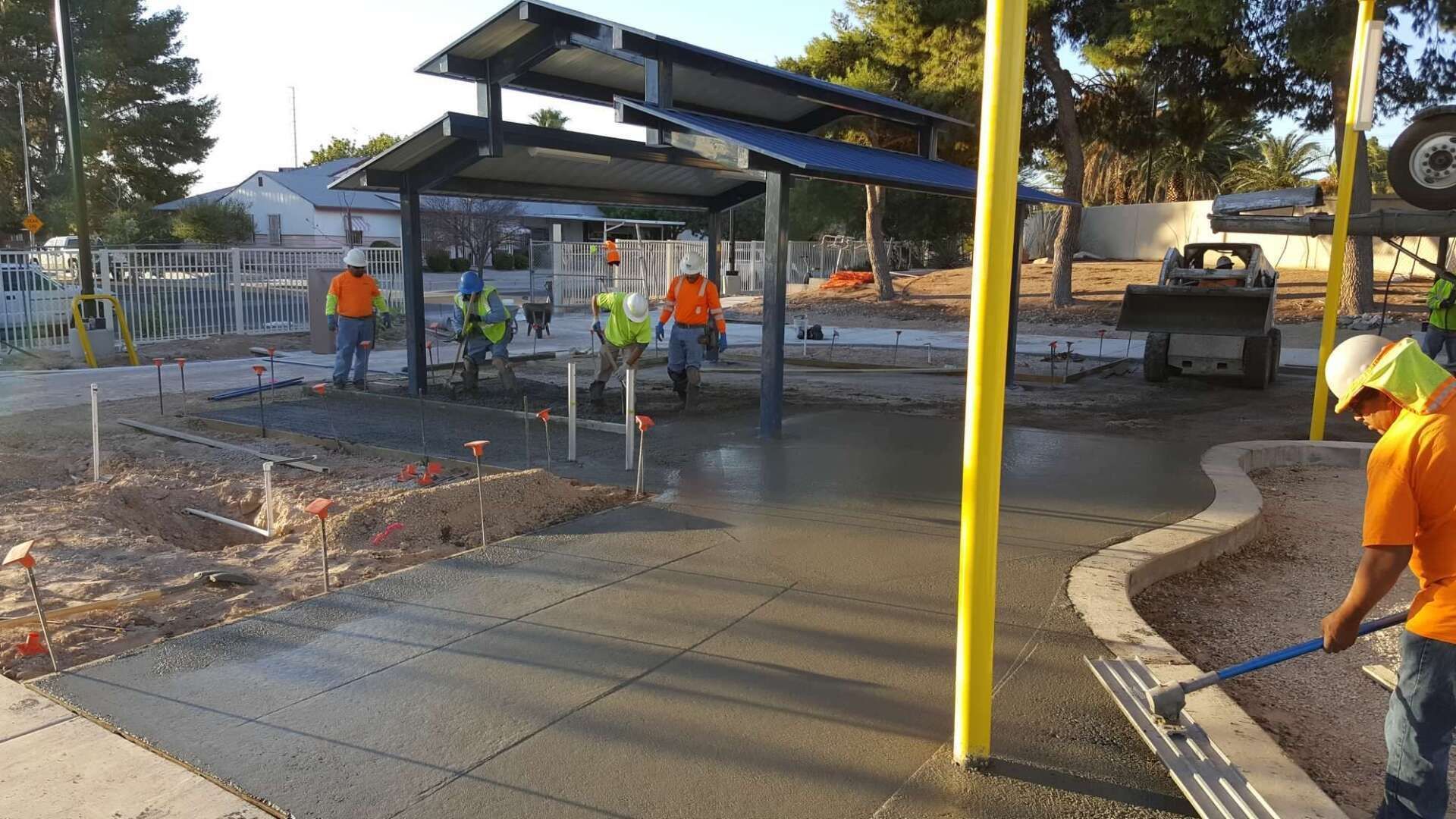 Construction workers pouring concrete at a park with solar panels overhead.