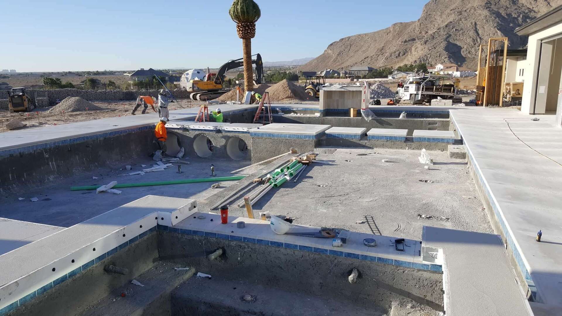 Pool construction site with machinery and piping; desert landscape in the background.