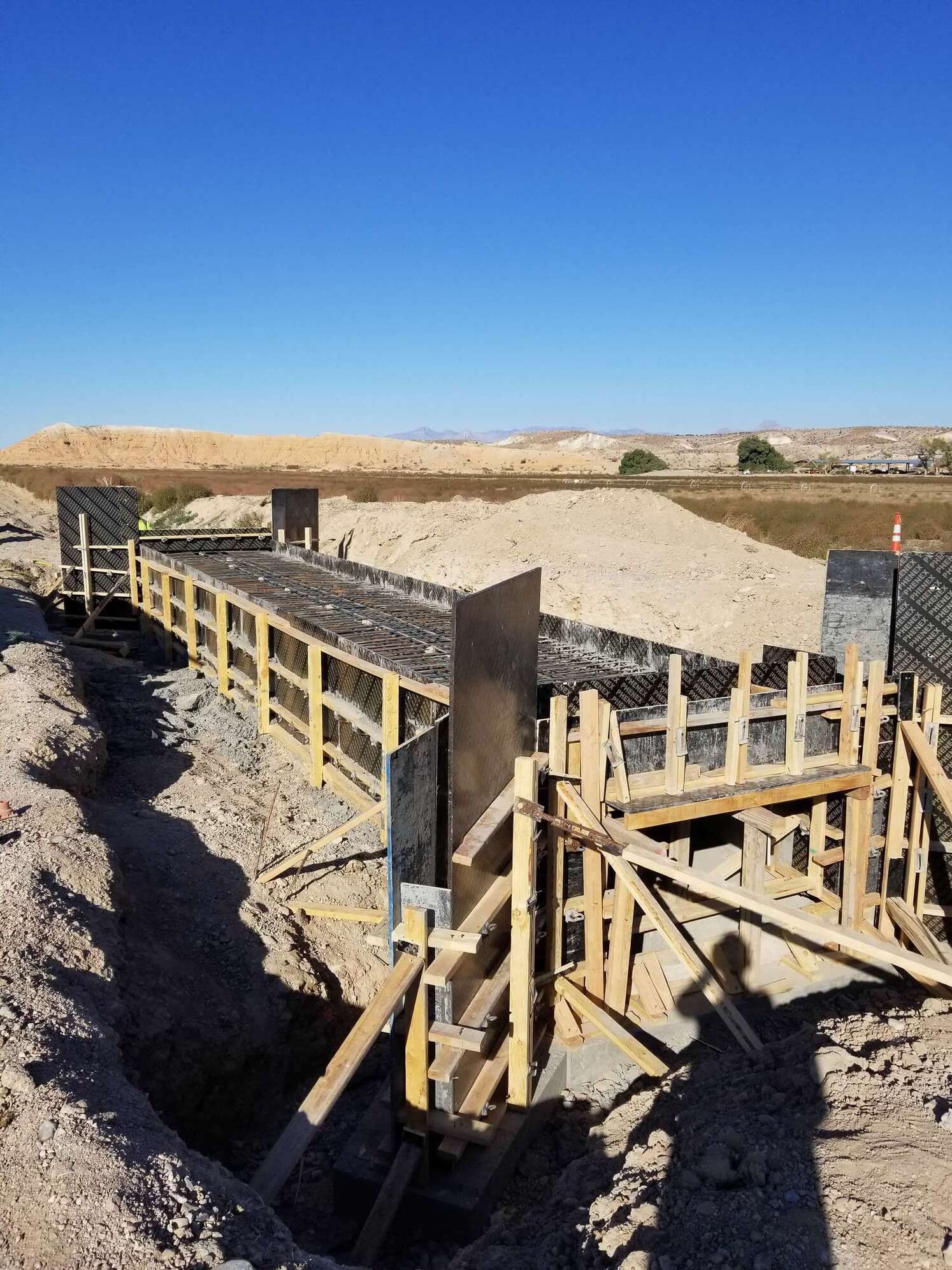 Construction site with wooden forms for concrete structure; trench, blue sky, earth tones.
