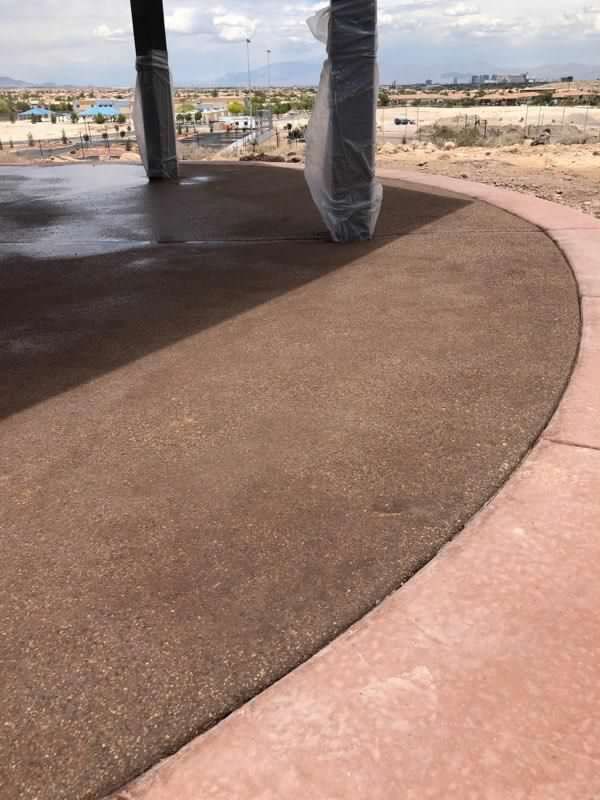 Brown concrete patio with a red border, columns, and a view of a park.