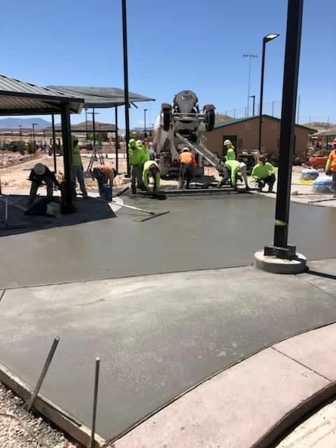 Construction workers pouring concrete at a park. A cement mixer is pouring, while workers smooth the surface on a sunny day.