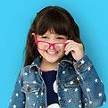 Jeune fille souriante, tenant des lunettes roses, vêtue d'une veste en jean à étoiles blanches. Fond bleu.