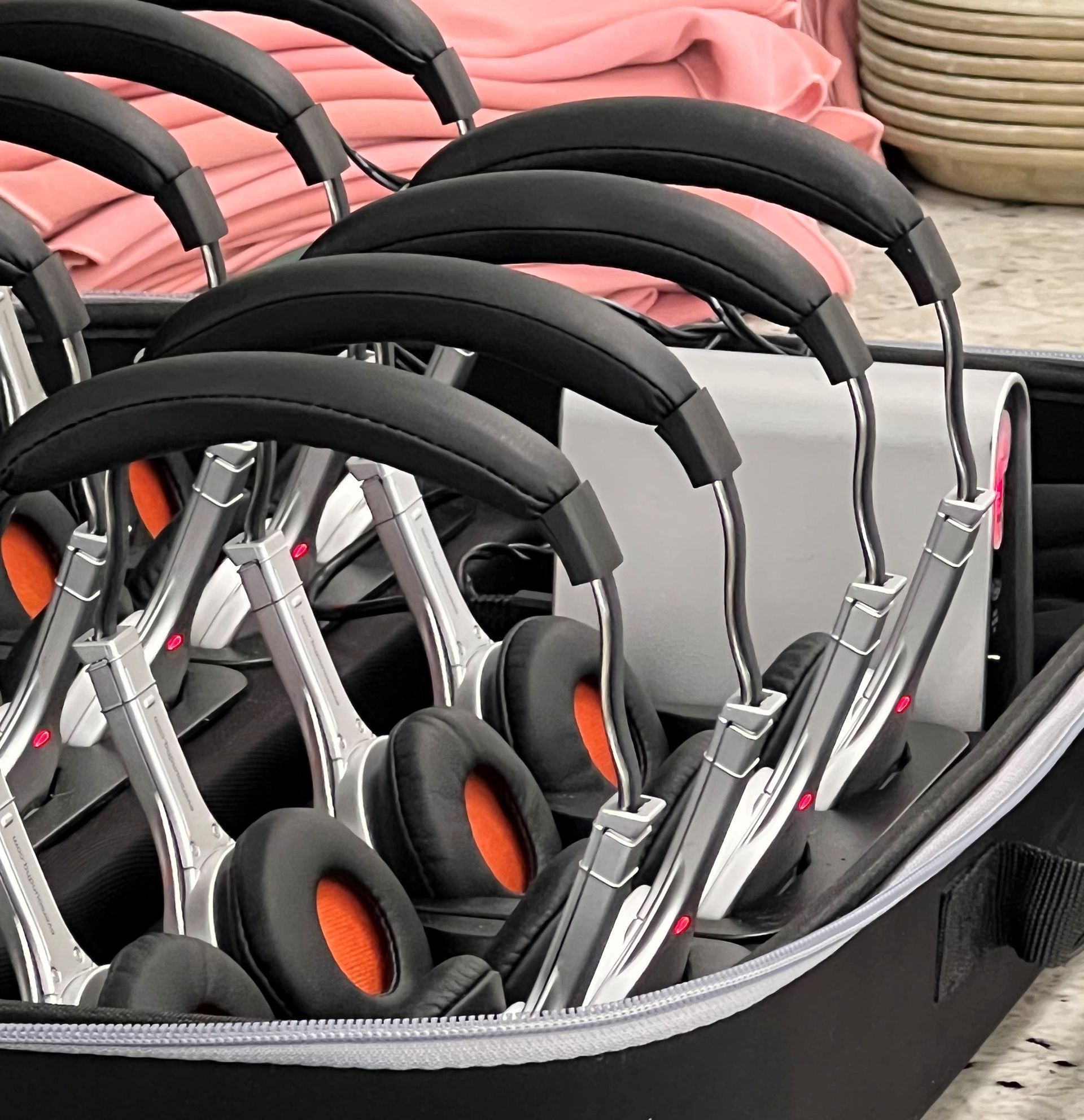 Headphones in a carrying case, silver and black, with orange ear padding.