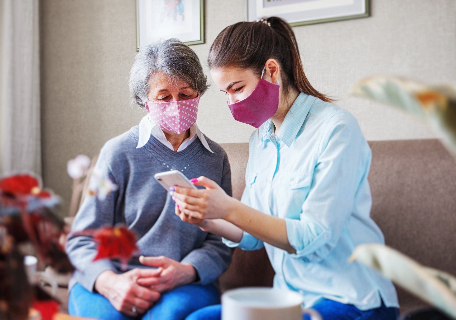 Woman showing phone to older woman; both wearing masks, indoors.