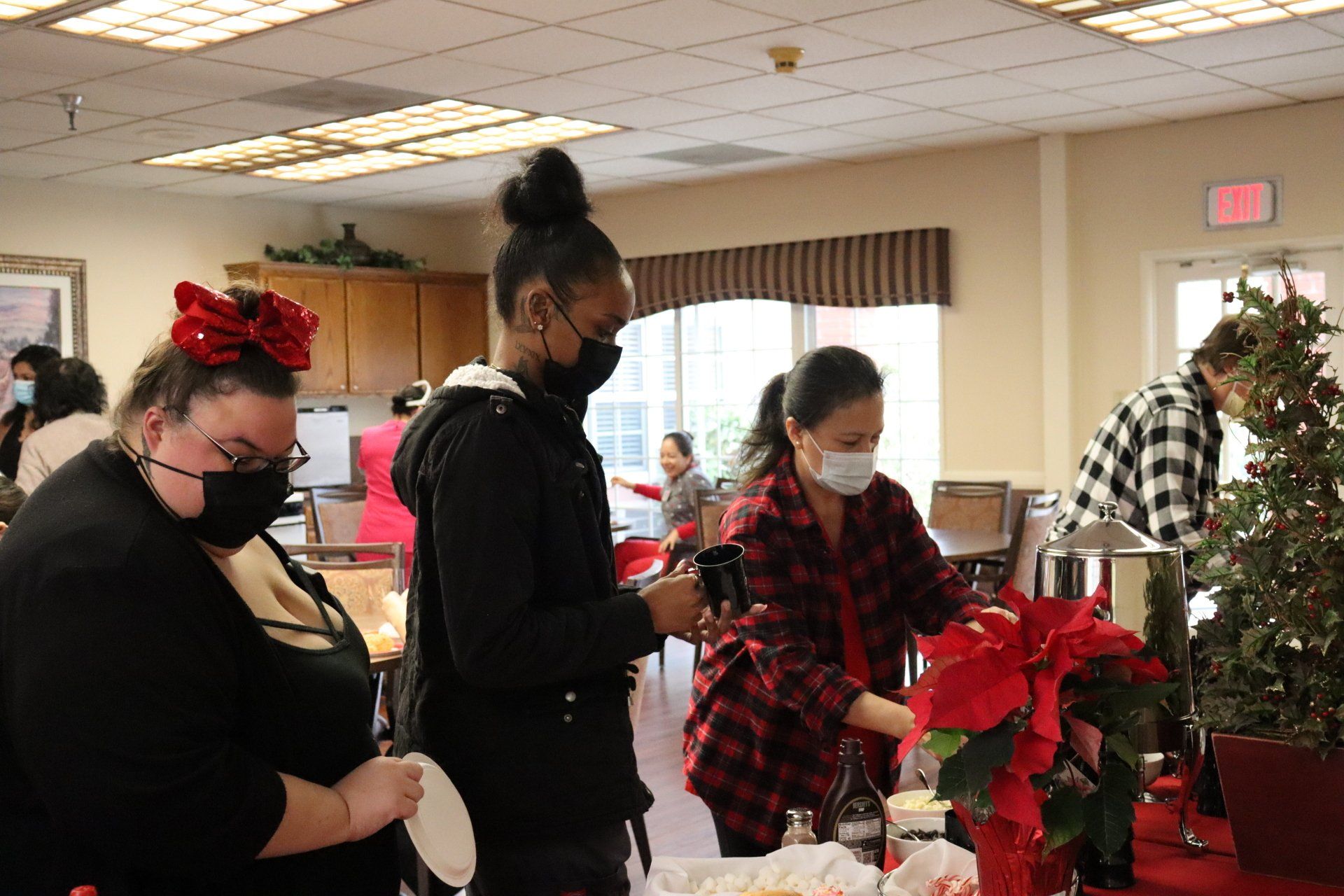 People in a room setting up decorations, wearing masks and holiday attire.