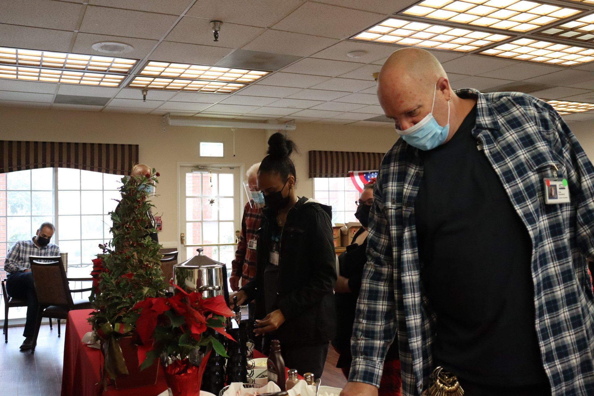 People at a gathering, some wearing masks, in a room with holiday decorations.