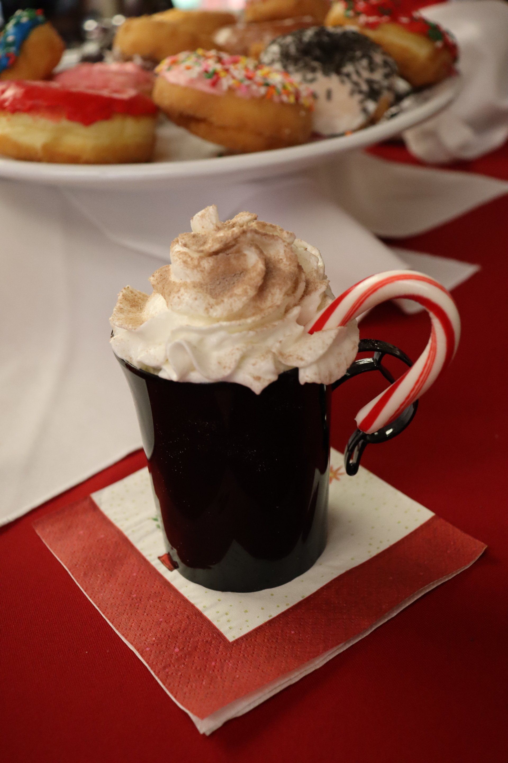 Hot chocolate with whipped cream and candy cane, donuts in the background.