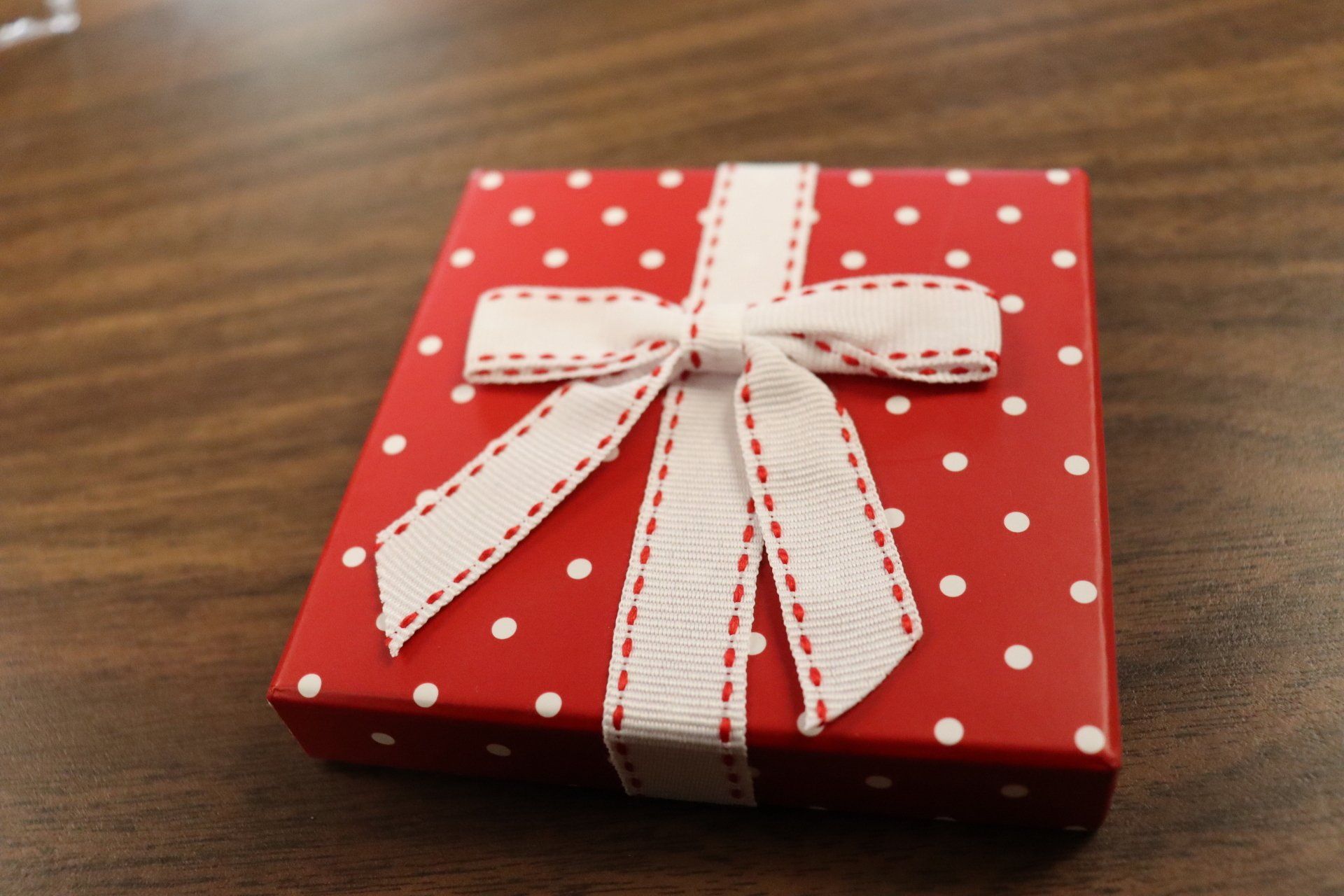 Red polka dot gift box with white ribbon and bow on a wooden surface.