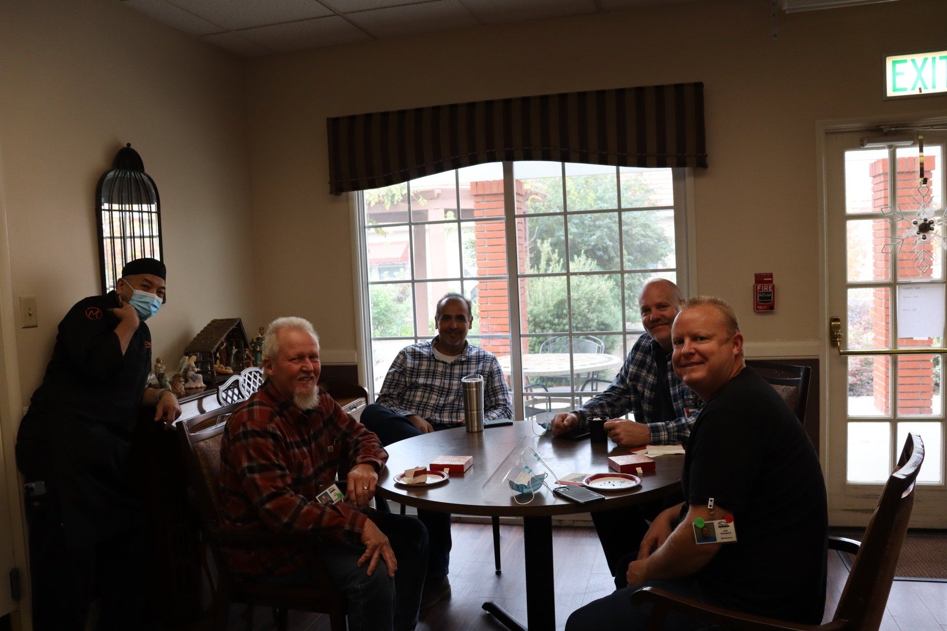 Six men sit around a table playing cards in a well-lit room, smiling.