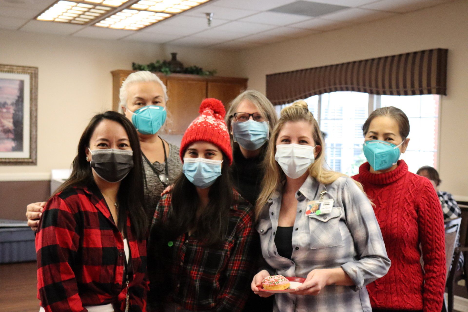 Group of six people wearing masks, posing indoors. Some wear festive hats/clothing.