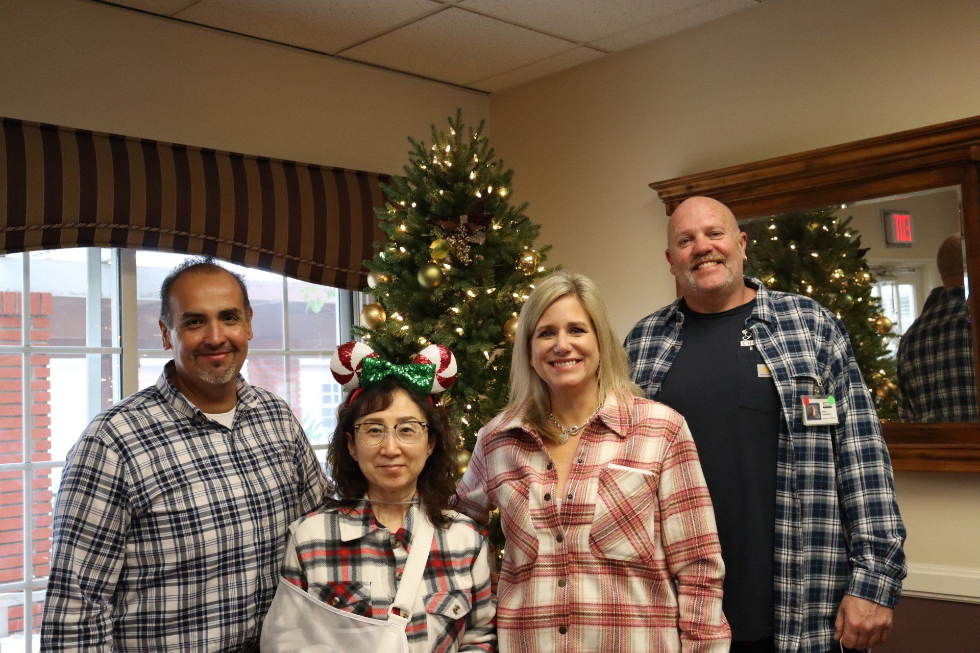 Four people in plaid shirts pose in front of a Christmas tree and window.