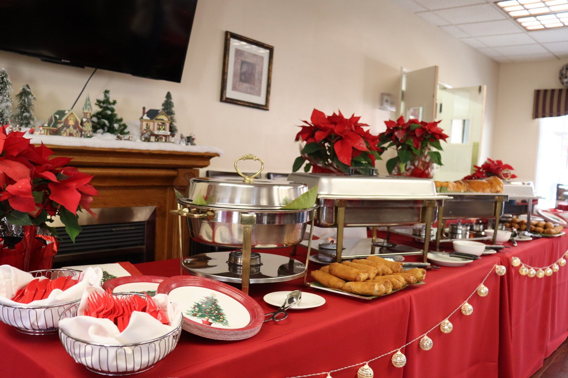 Buffet table with Christmas decor: red tablecloth, poinsettias, chafing dishes, plates, and food.
