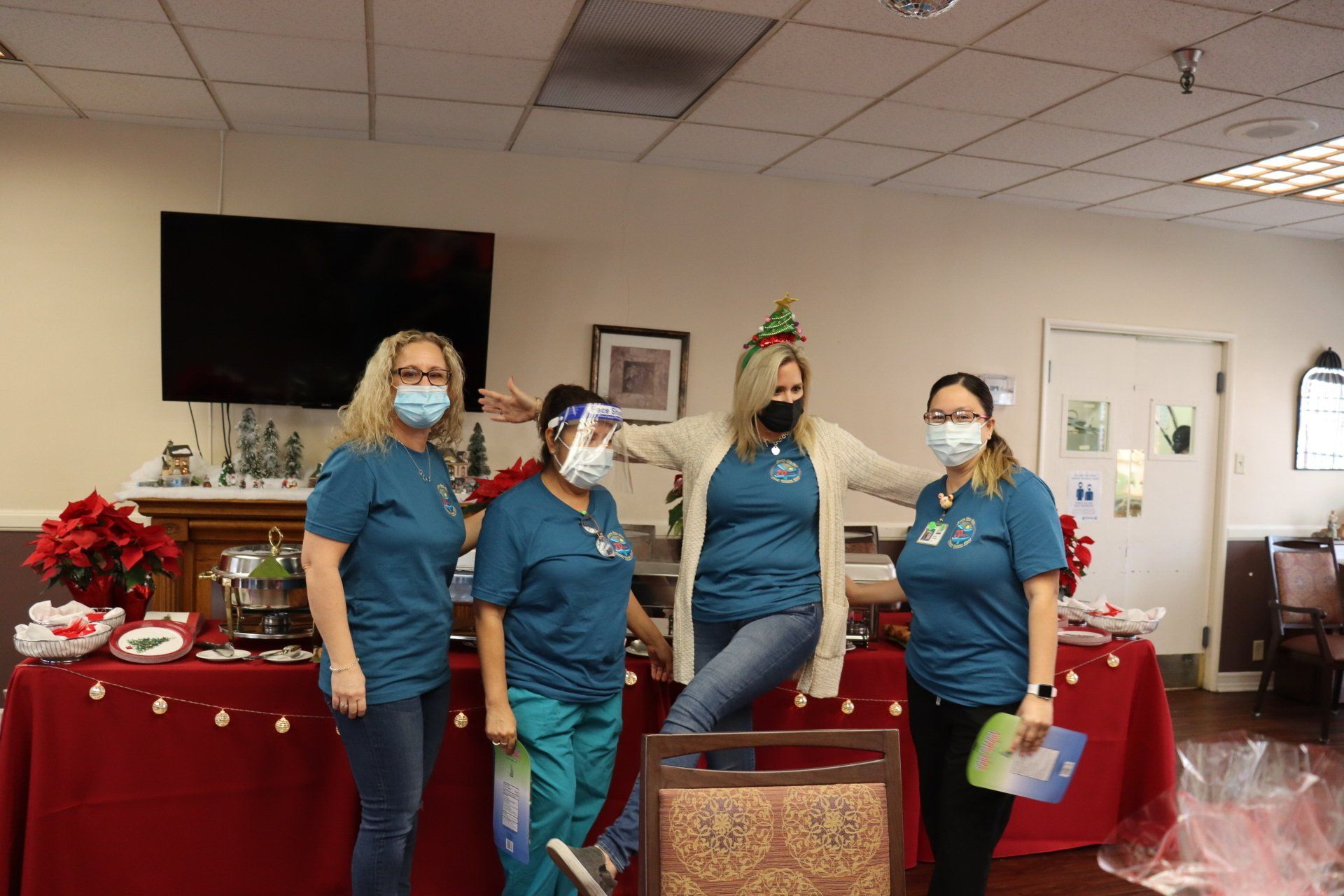 Four healthcare workers pose near a holiday display, all wearing masks, one with a face shield.