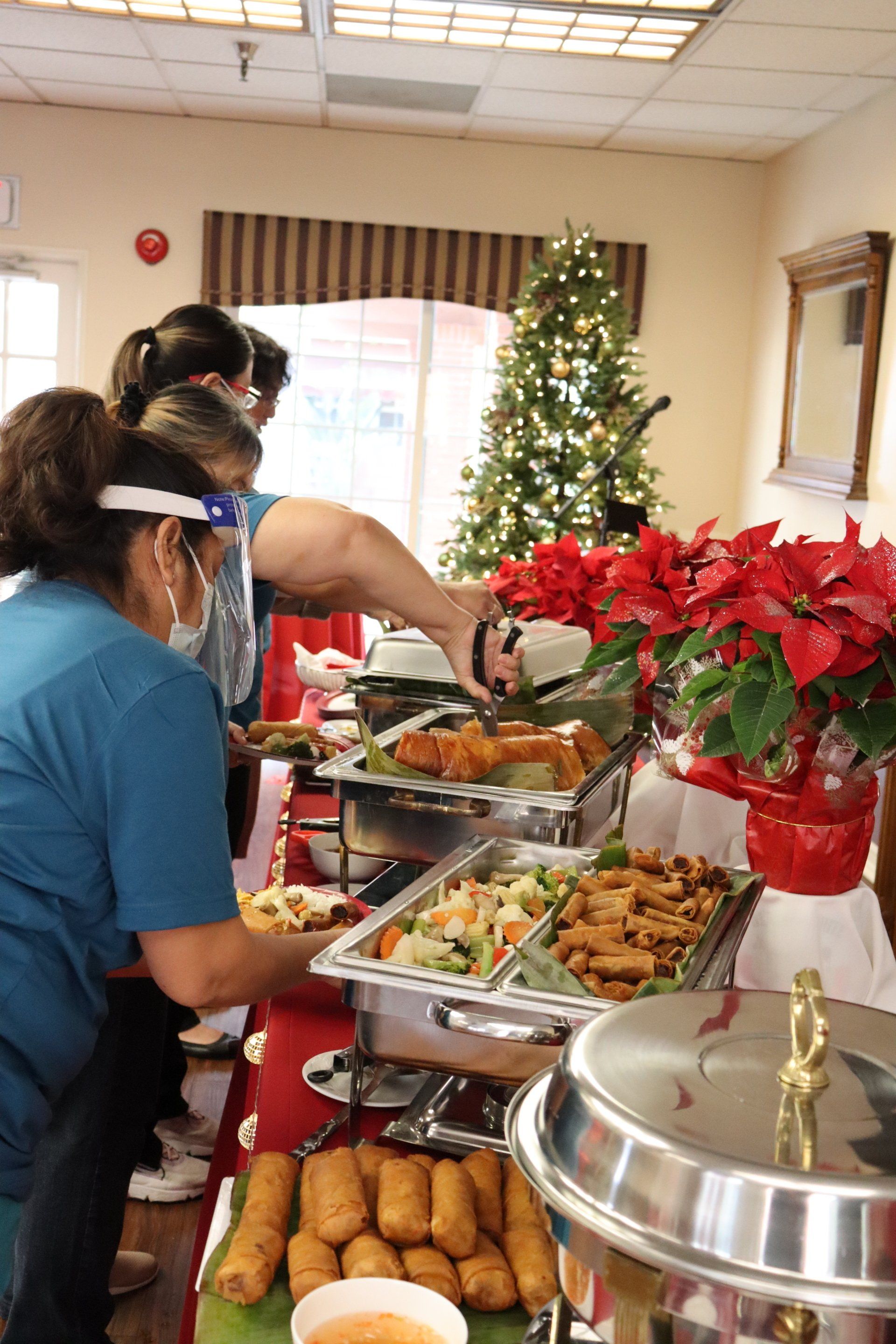 Buffet table with people serving food. Christmas tree and poinsettias in the background.