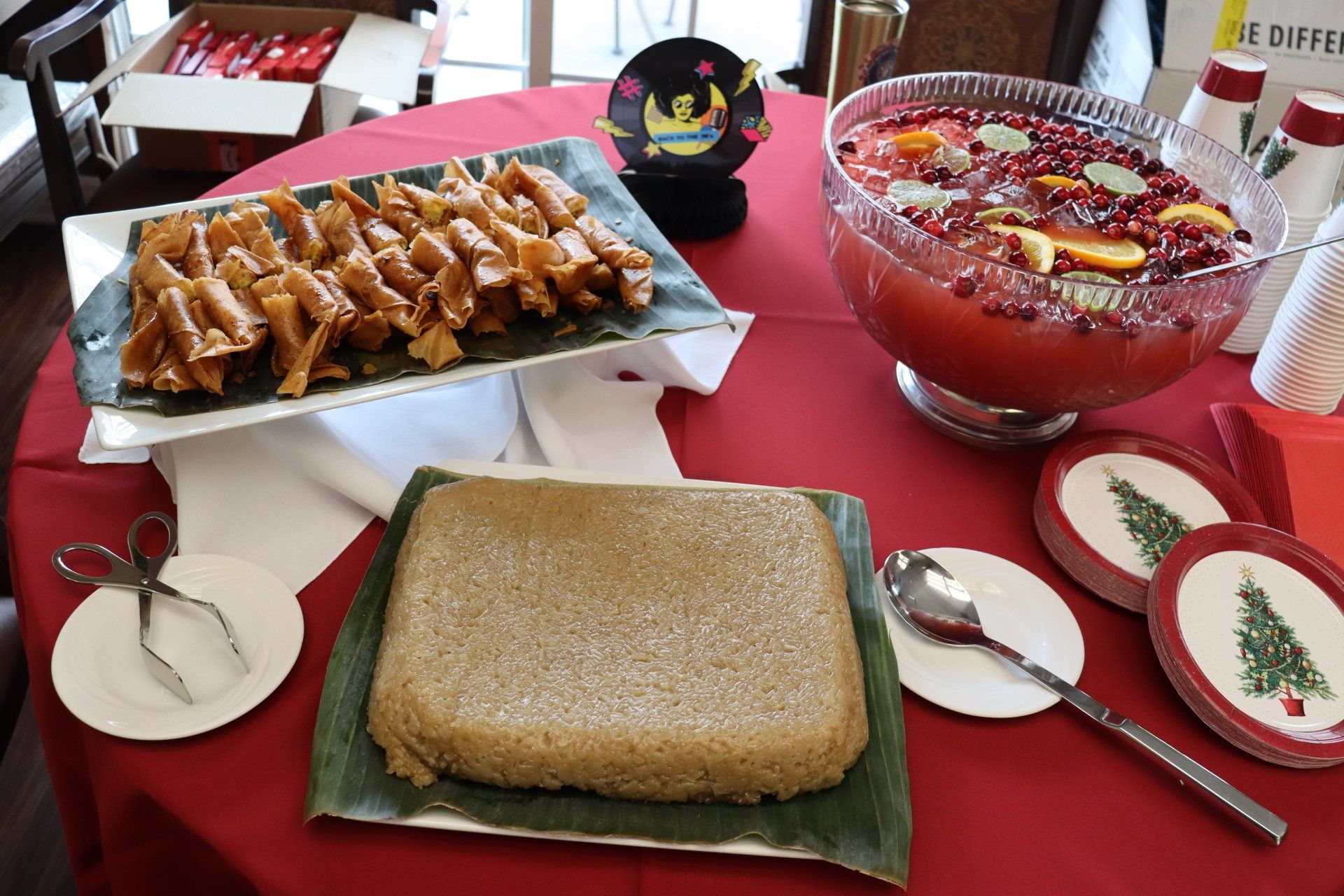 A table with food and punch. Dishes include pastry, cake, and a fruit-filled punch bowl. Christmas plates.