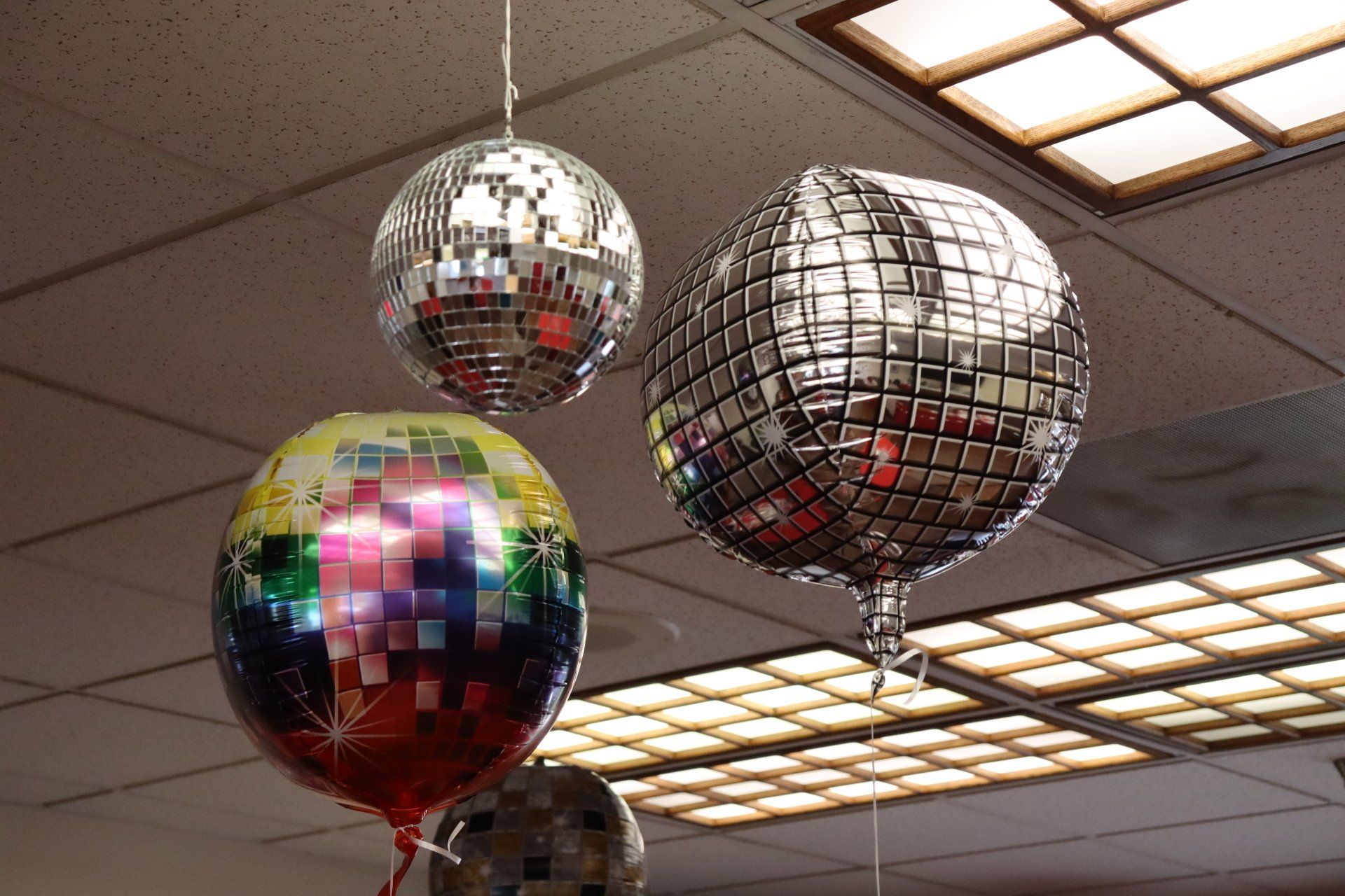 Three disco ball balloons hanging from the ceiling in a room, reflecting light.