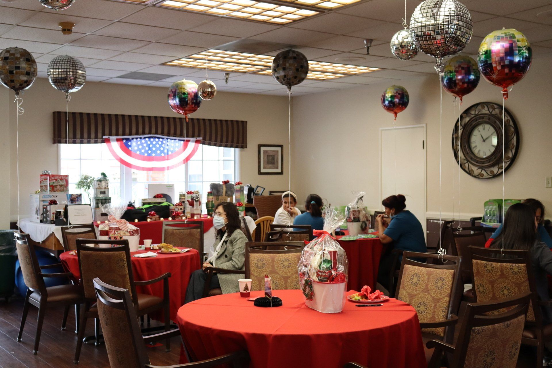 Party room with red tablecloths, balloons, and people sitting at tables.