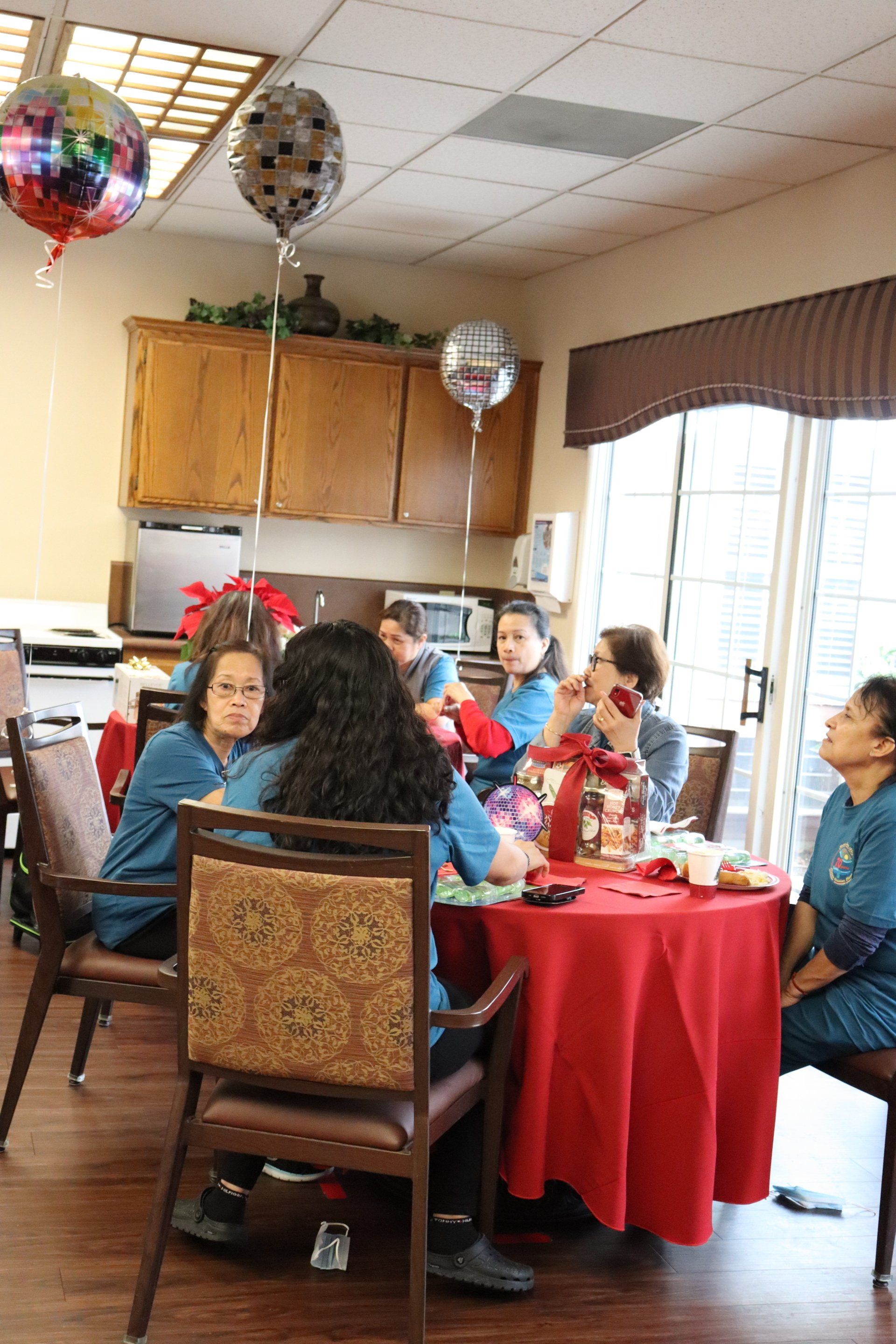 Group of people in blue shirts gathered around a red table, balloons, celebrating indoors.