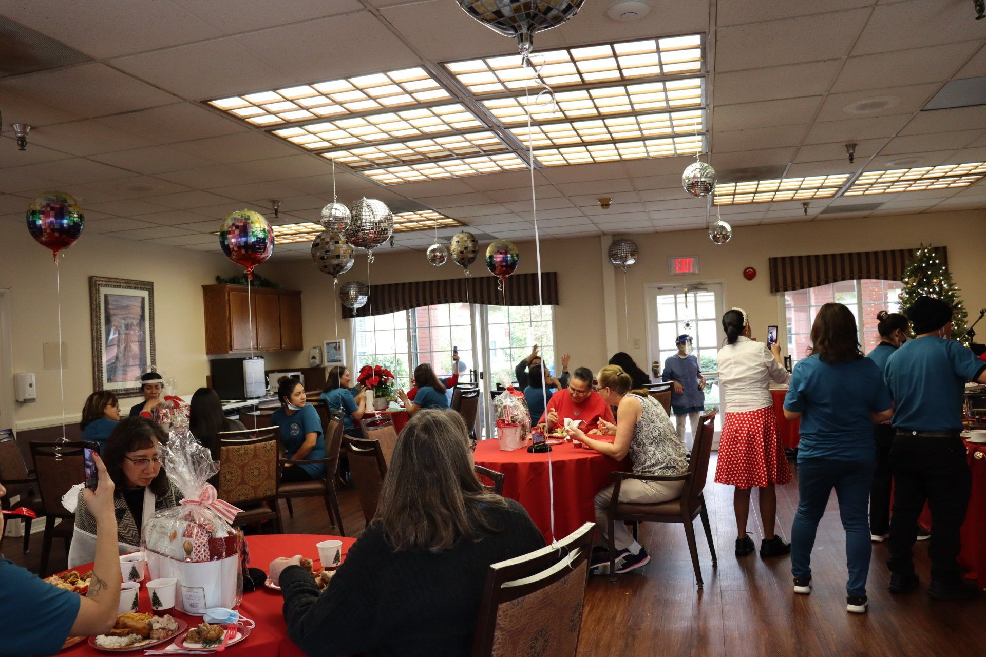 People at a party in a room with red tables, decorations, and balloons.