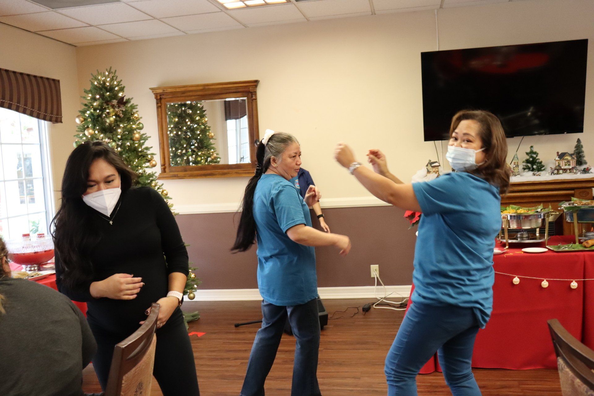 Three women wearing masks dancing in a decorated room, possibly a Christmas party.