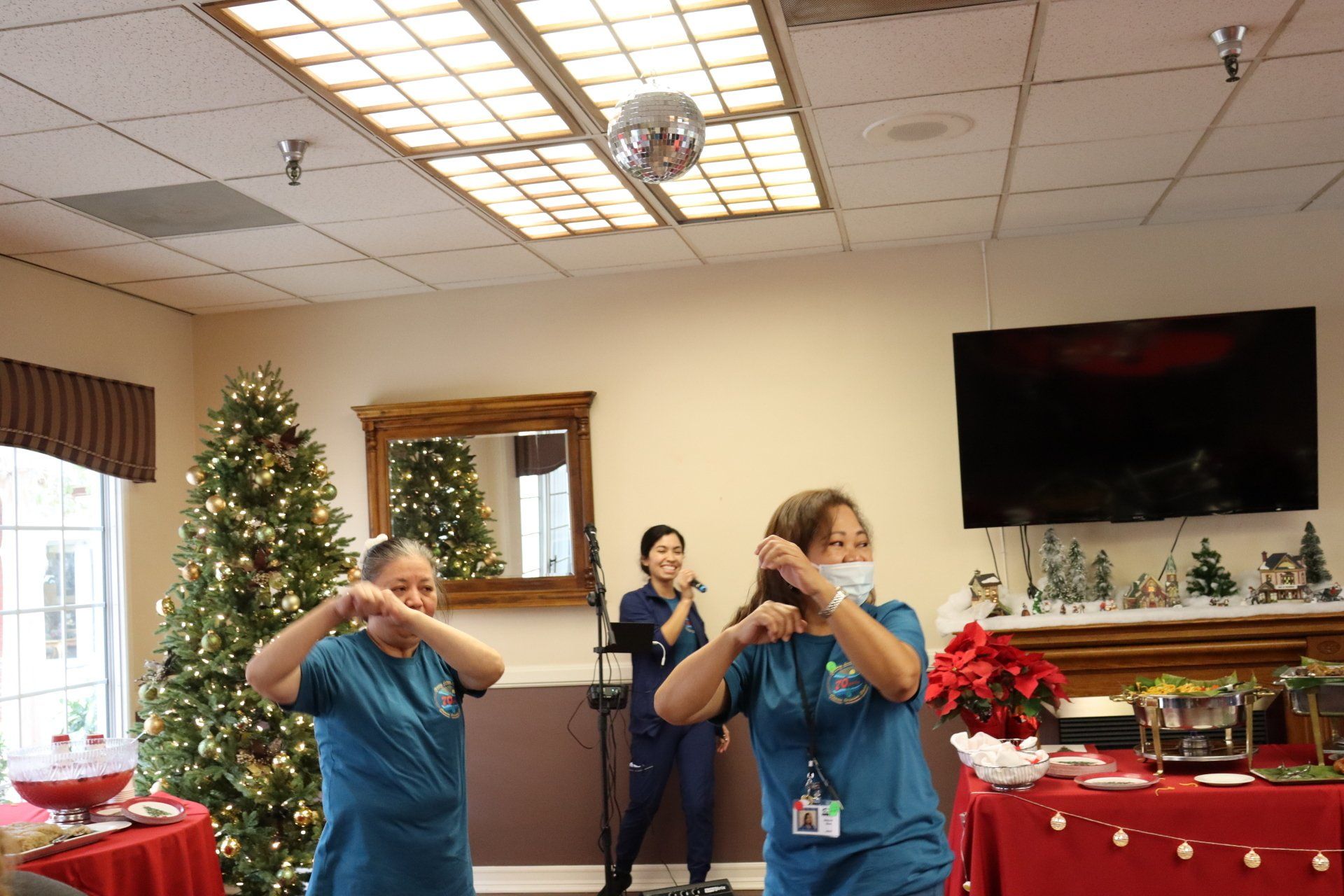 Two healthcare workers dance with a singer, next to a Christmas tree.