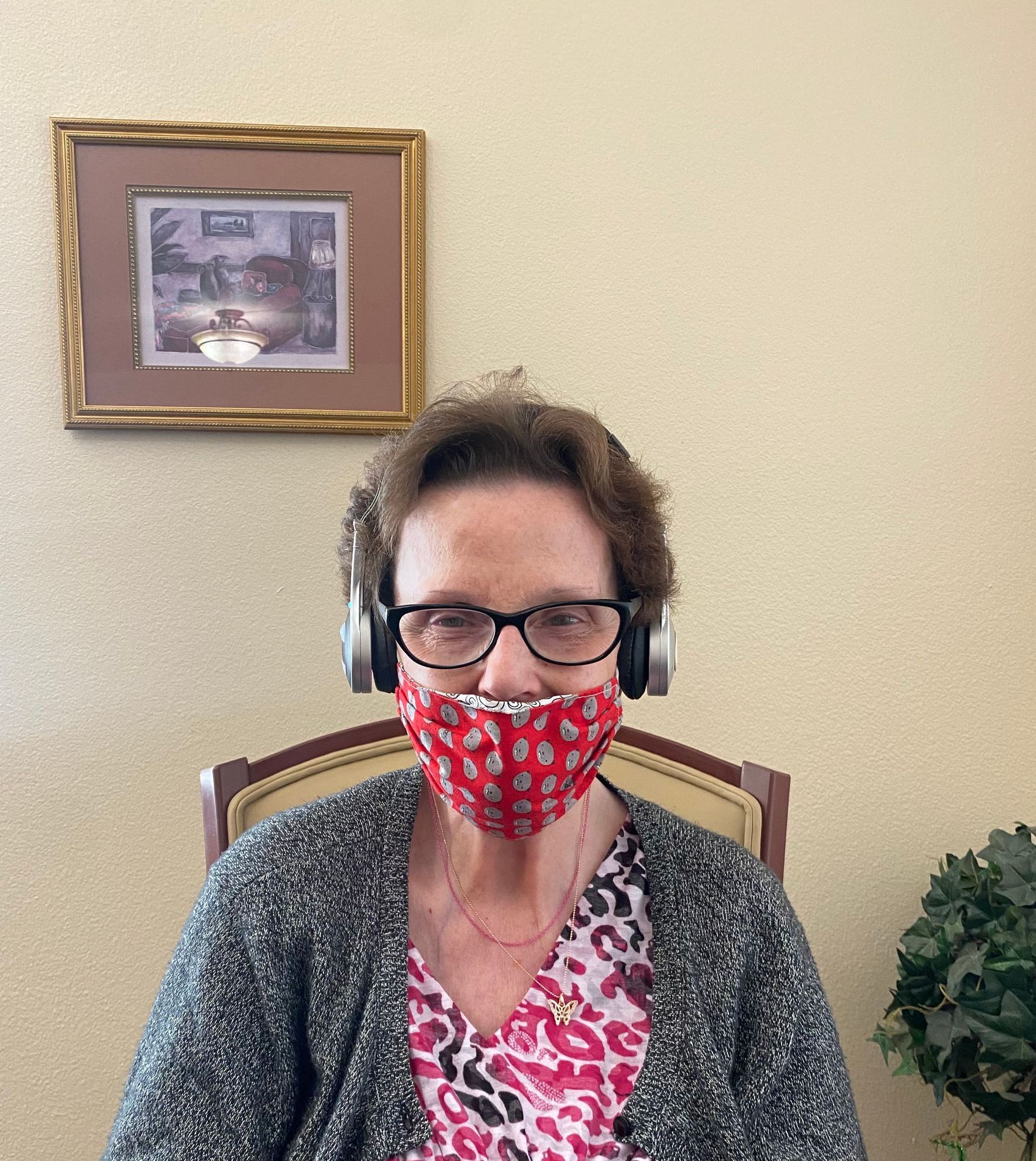 Woman wearing a mask and headphones indoors. She has glasses and is sitting in a chair.