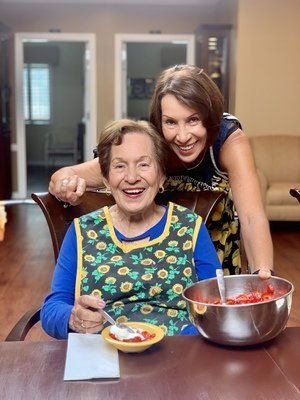 Woman and older woman smiling; older woman eats dessert, bowl of strawberries on table.