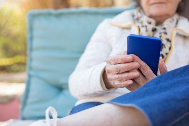 Elderly woman using a blue smartphone while sitting outdoors.