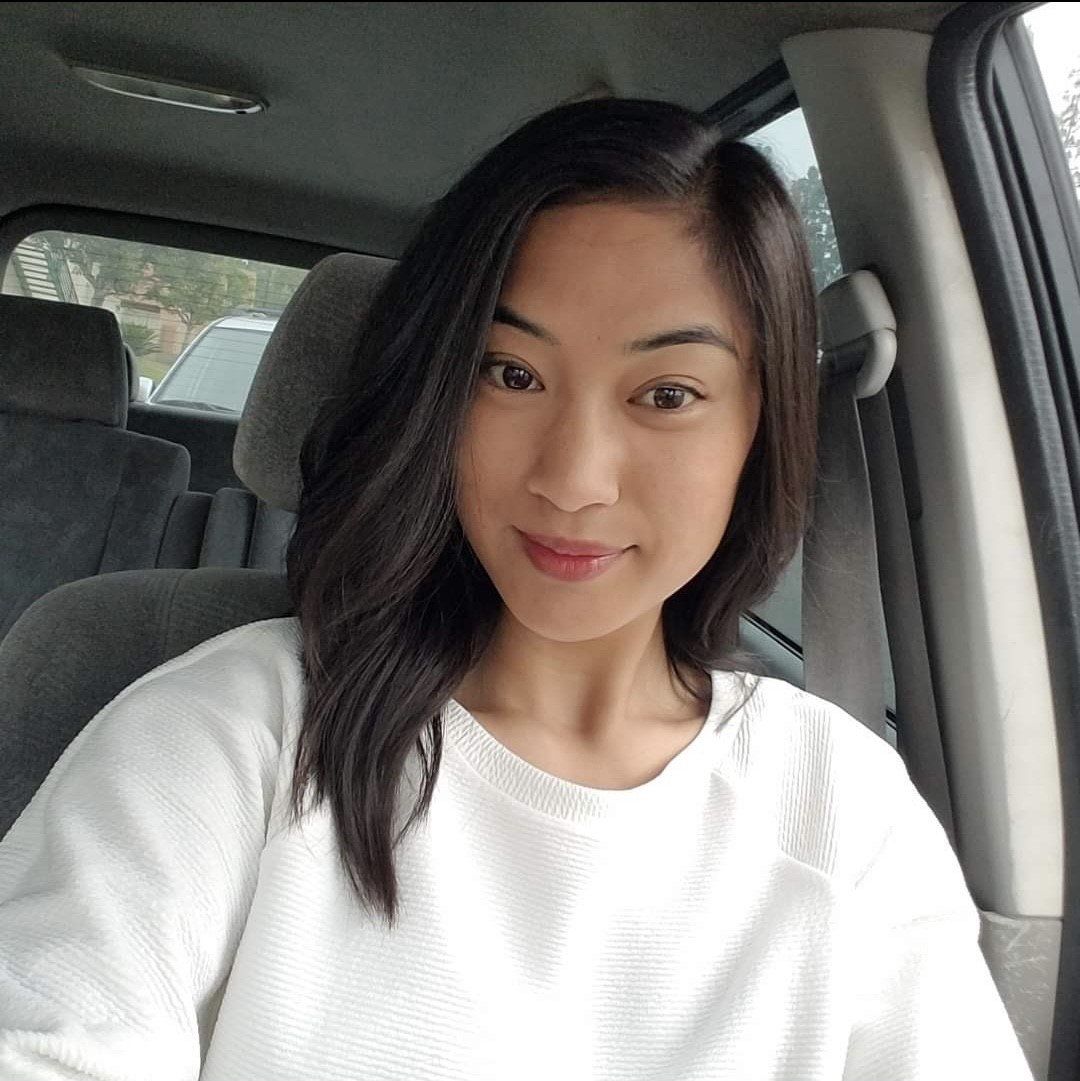 Woman with dark hair in a white sweater smiles while sitting inside a car.