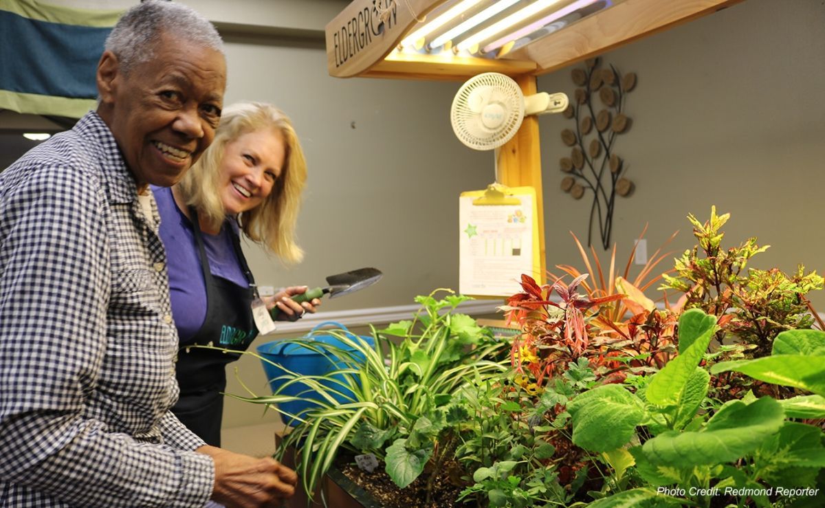 Man and woman smile at a small indoor garden with plants. The man touches the plants.