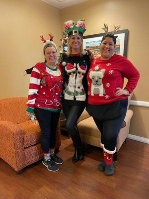 Three people in Christmas sweaters pose for a photo in a room with a couch, antlers, and festive accessories.