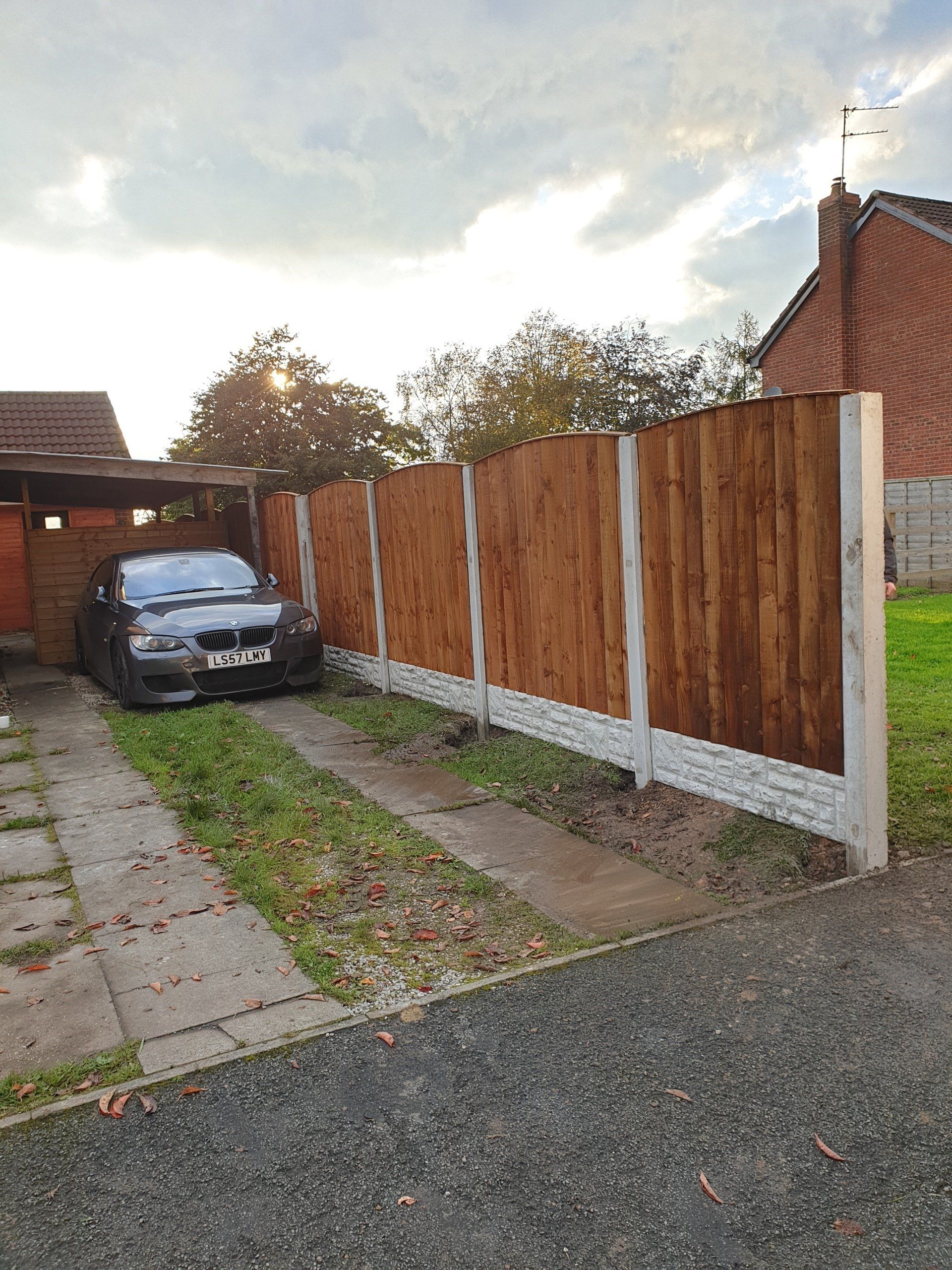 Wooden fence with a car parked beside it on a driveway.