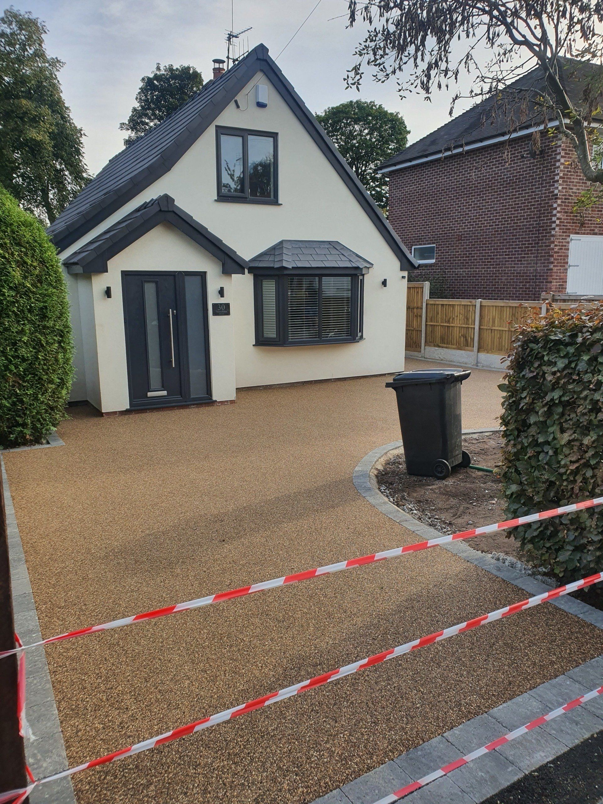 Curb-appeal view of a house with a gravel driveway, gray roof, dark trim, and a black trash can.