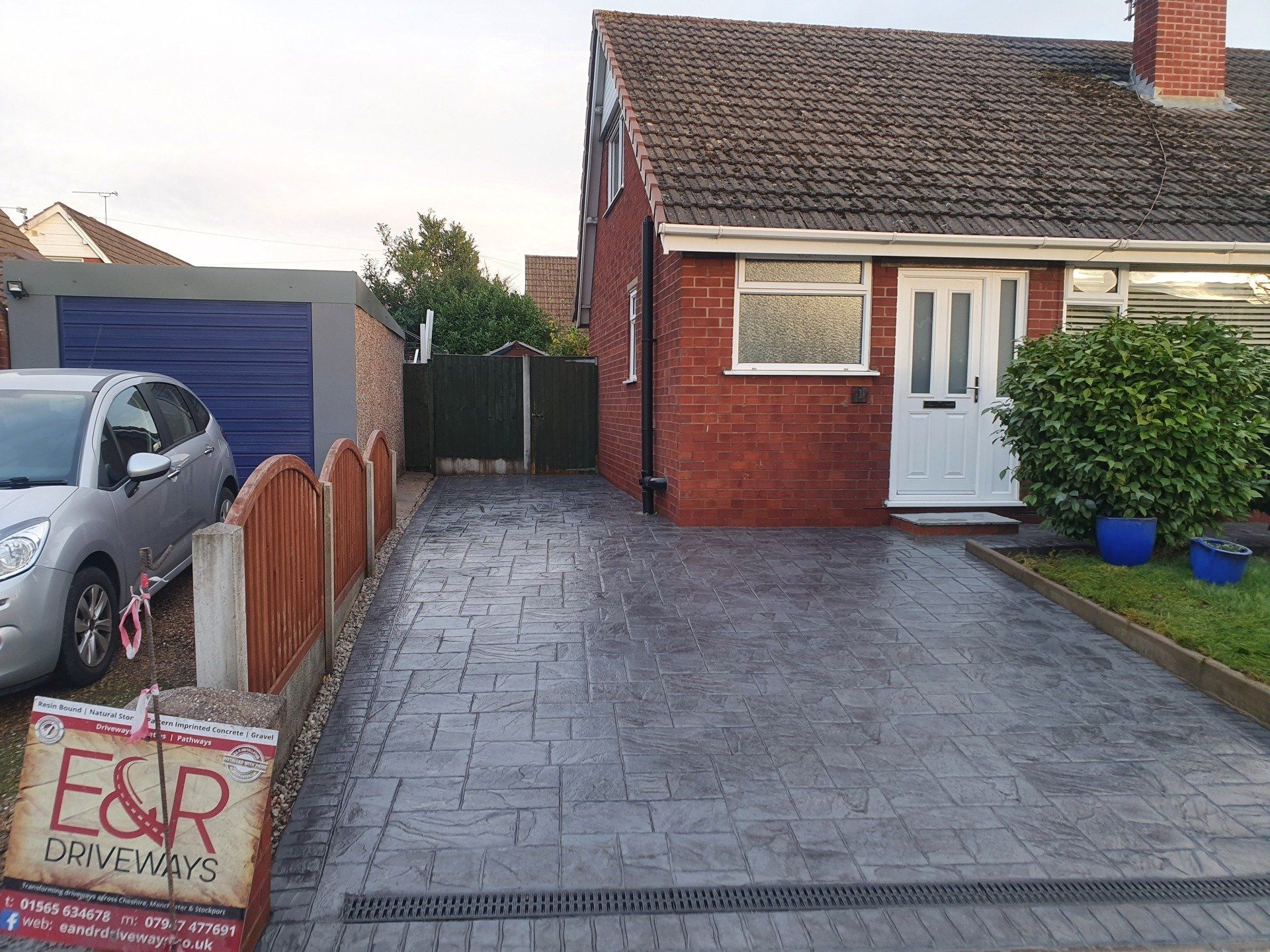 Gray stamped concrete driveway with a brick house and a silver car.