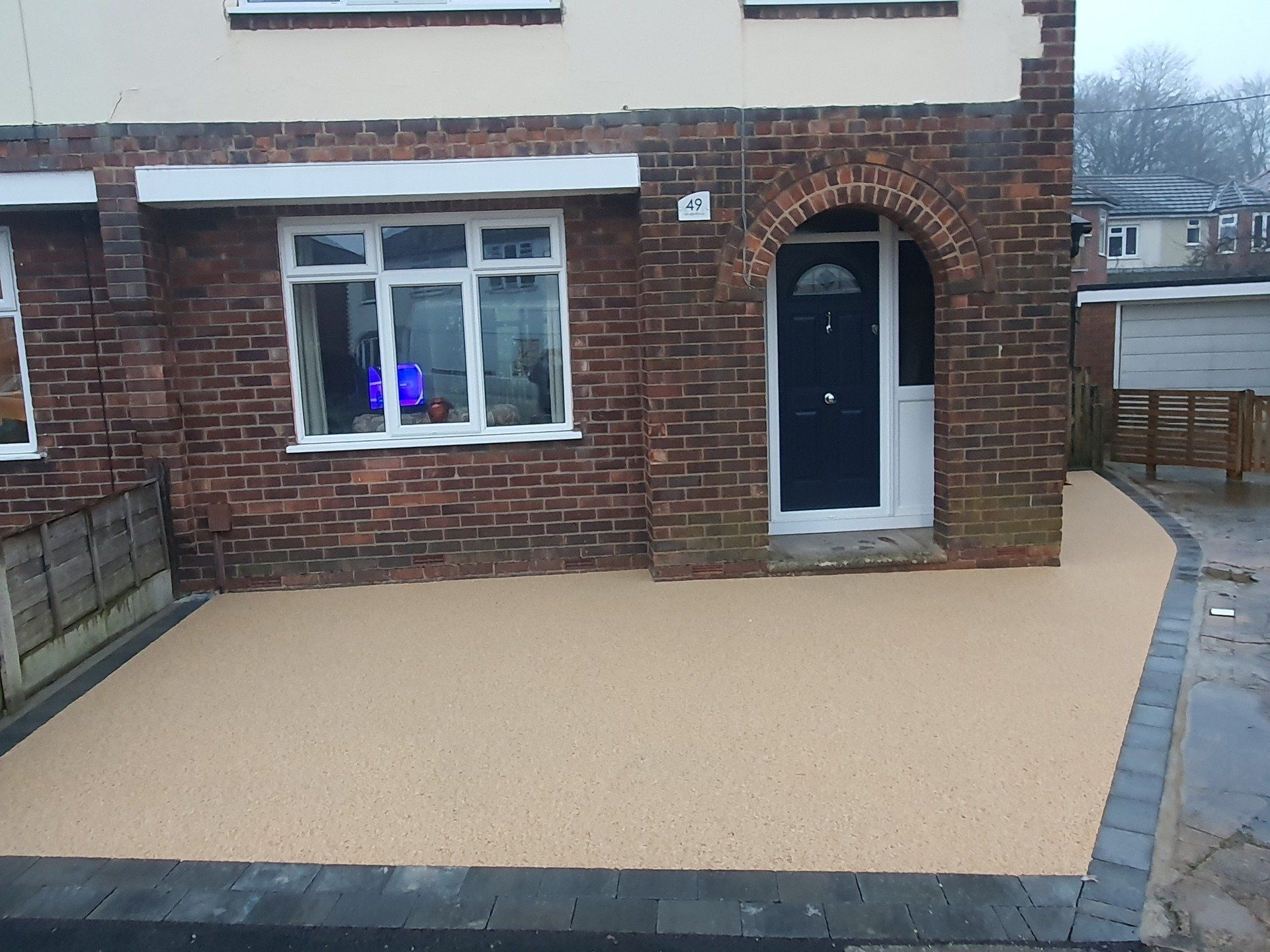 Brick house with black door, tan driveway, and brick and gray borders.
