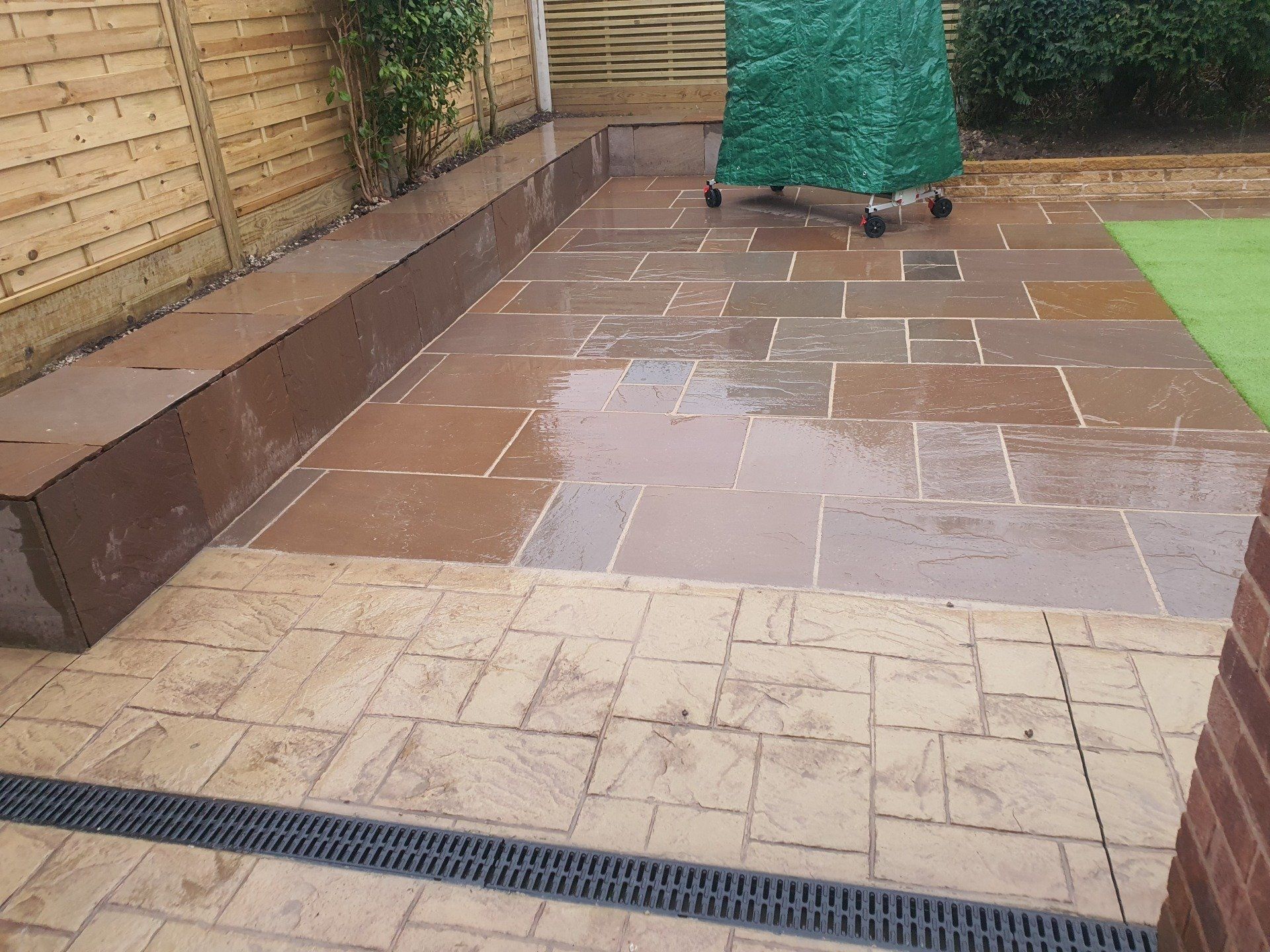 Brown patio with wet stone tiles, a dark border, and a covered grill.