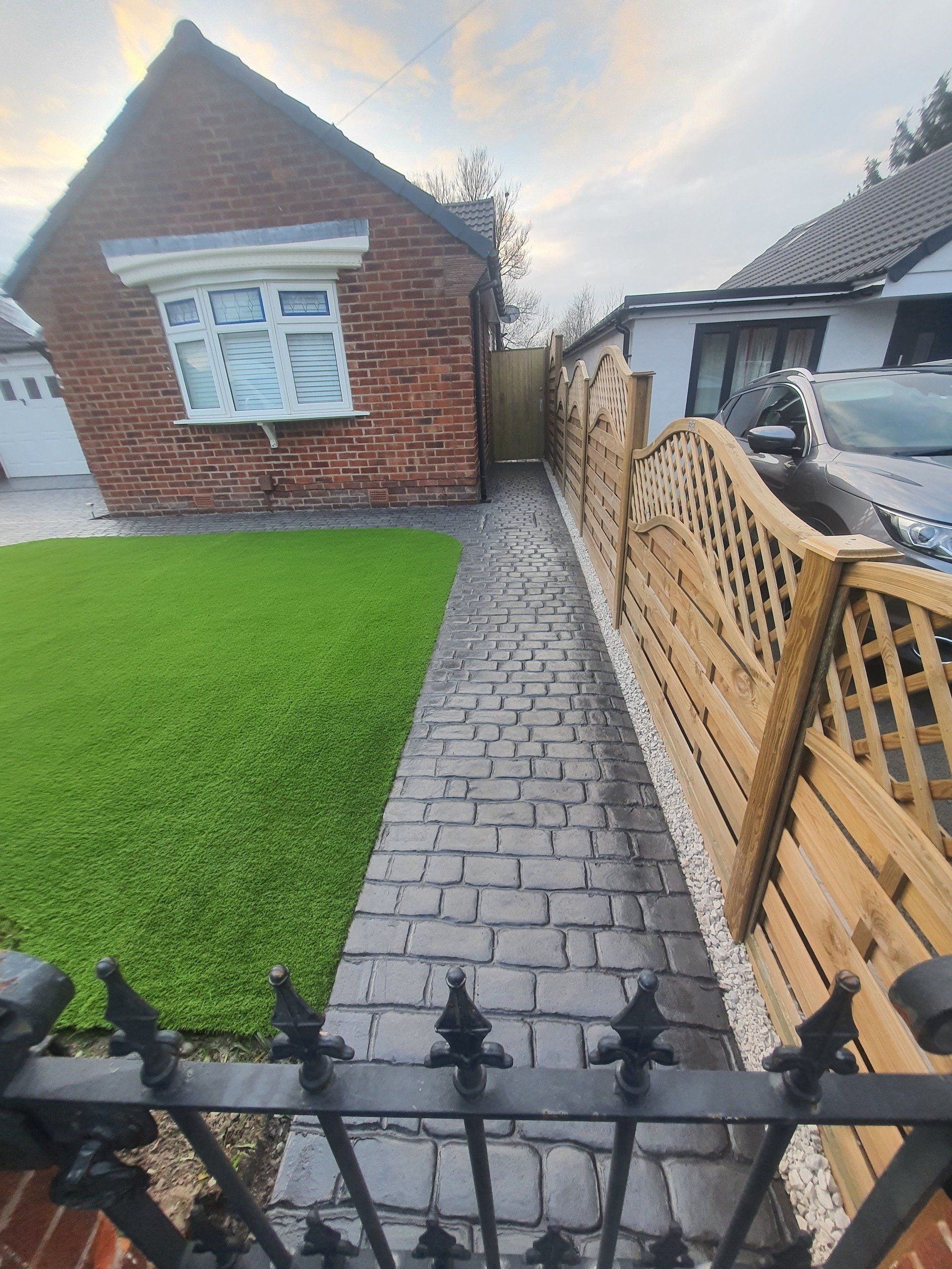 Brick home with green lawn, paved path, and wooden fence.