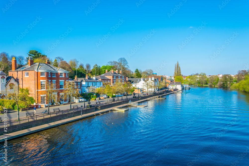 Riverfront buildings under a clear blue sky. A steeple is visible in the distance.