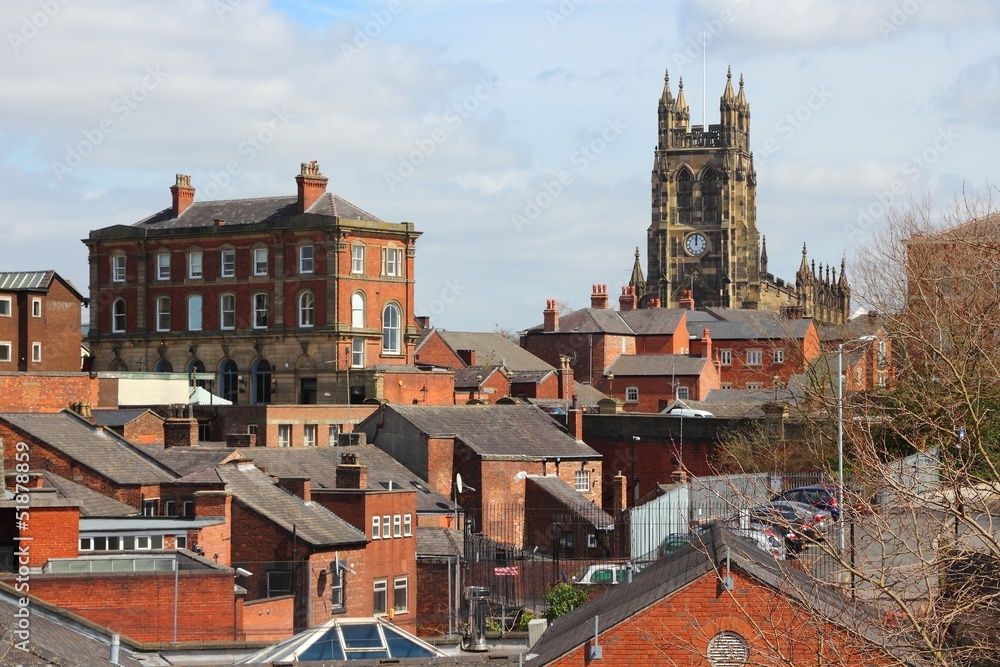 View of red brick buildings and church tower under a blue sky.