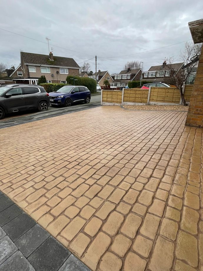 Brick paved driveway with parked cars and wooden fence on a cloudy day.