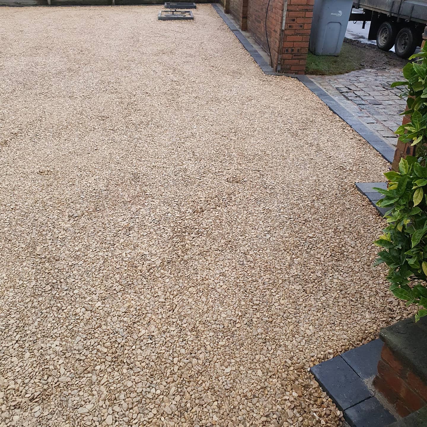 Gravel driveway with tan-colored stones, bordered by dark gray edging and a red brick wall.