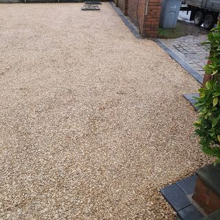 Gravel driveway edged with dark gray borders, next to a brick wall and sidewalk.