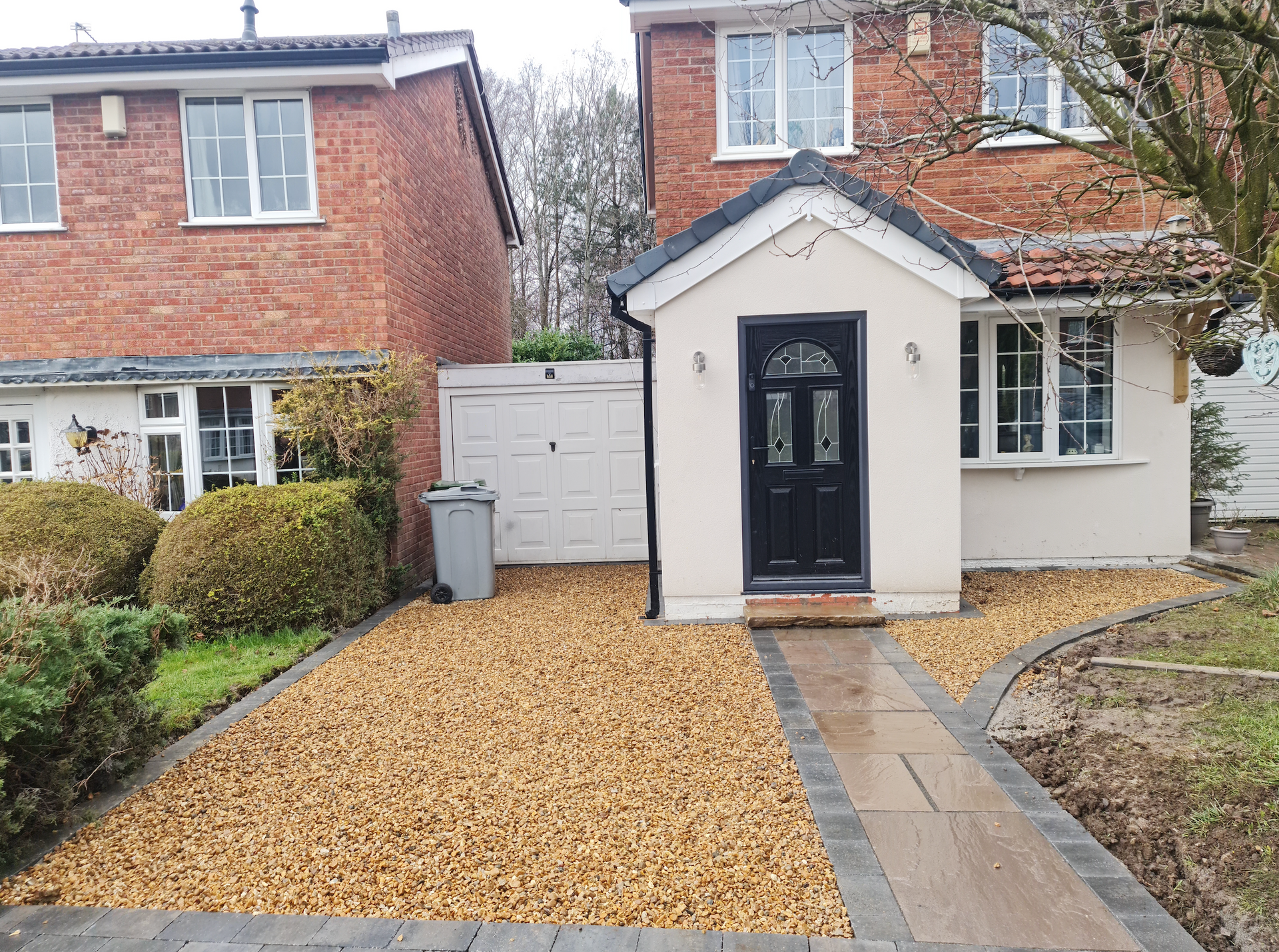Gravel driveway and paved walkway leading to the front door of a two-story brick home with a small porch.