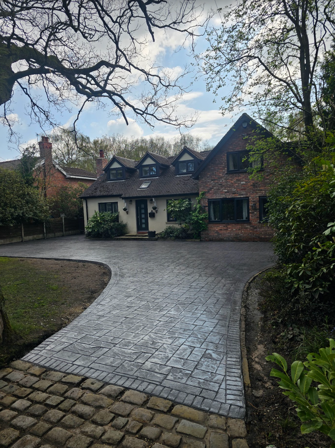 Brick house with driveway, trees, and cloudy sky.