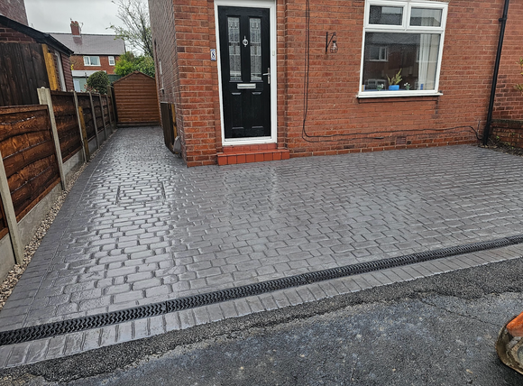 Brick home with a paved driveway, front door, and a drainage system.