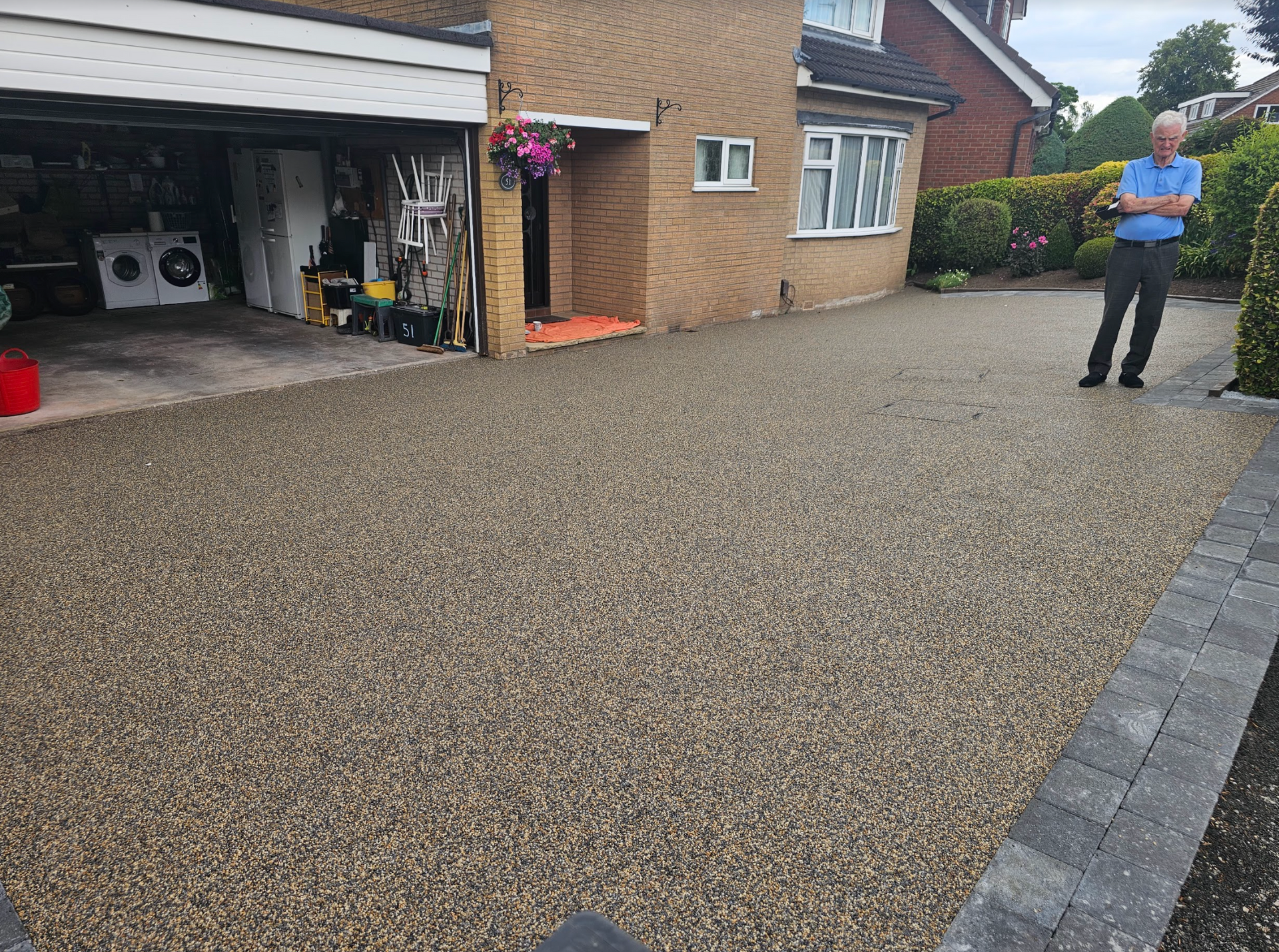 Gravel driveway in front of a brick house. A man stands on the right side. Garage on the left.