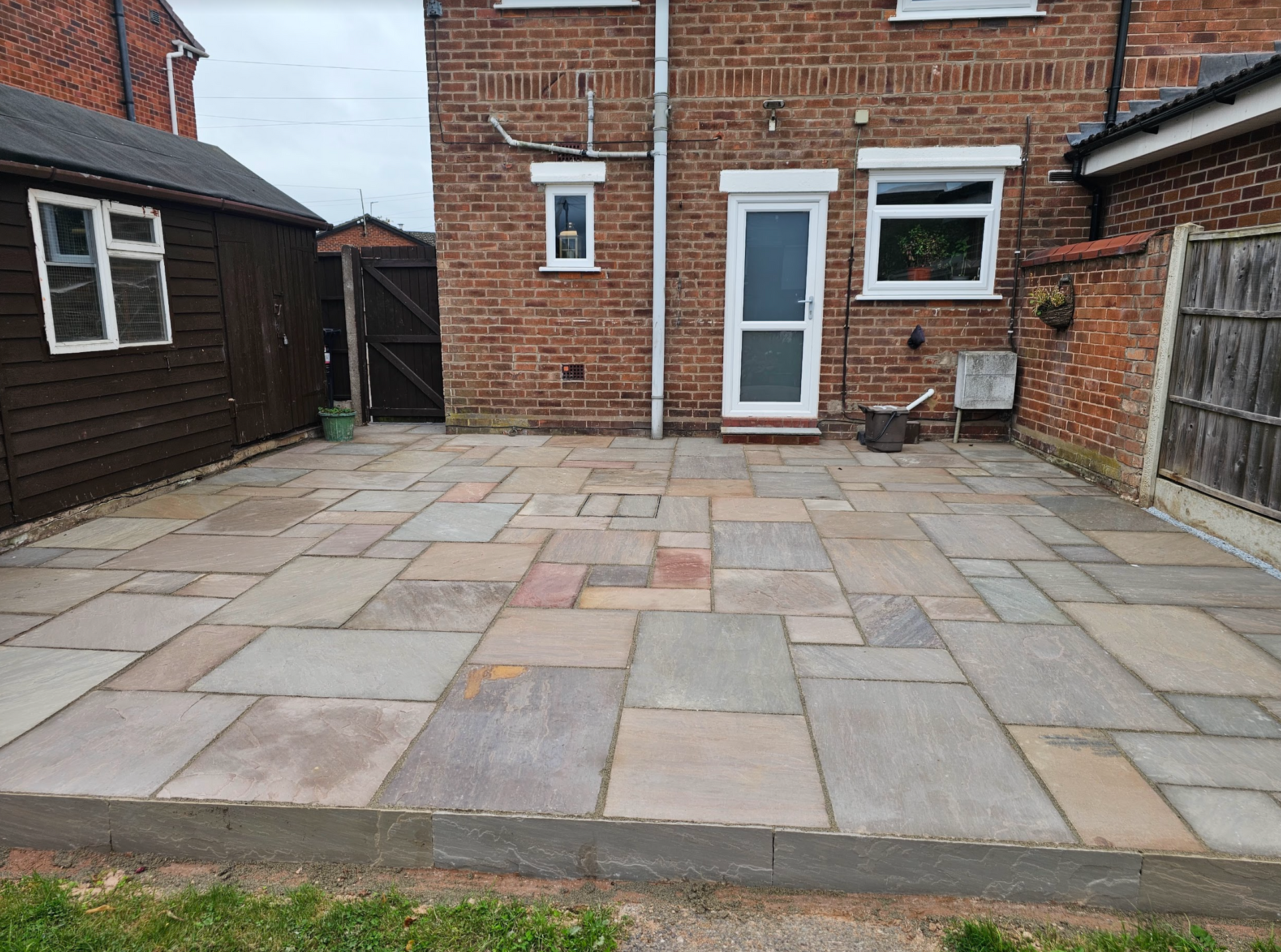 Stone patio in a backyard with a brick house and wooden shed.