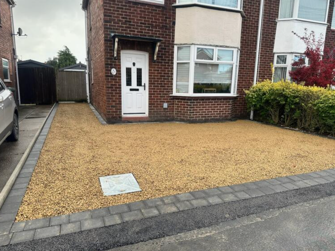 Gravel driveway in front of a brick house with a white door and a small porch.