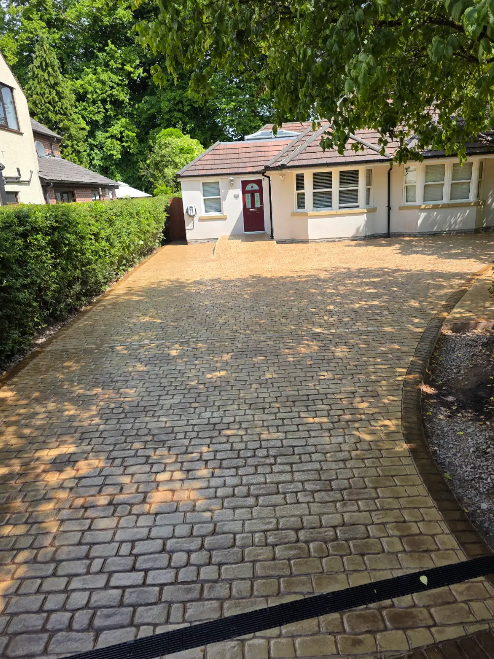 Driveway of a bungalow with a brick pattern. Beige and brown bricks with a hedge on the left.