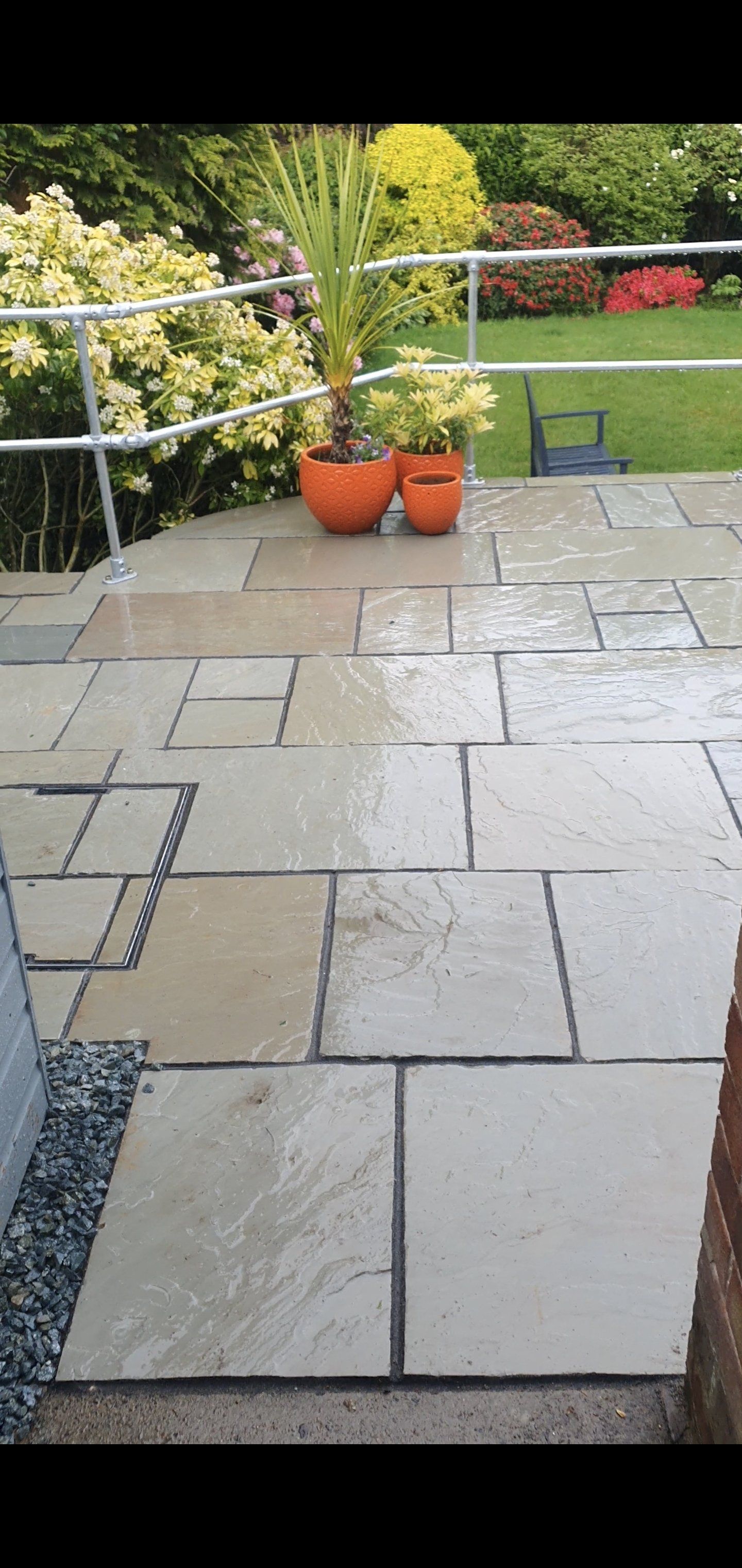 A wet patio with stone tiles. Two orange pots with plants. A grassy yard is in the background.